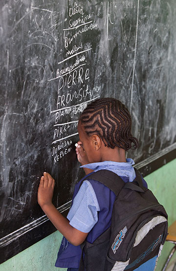 I child writing on a chalkboard with a backpack on.